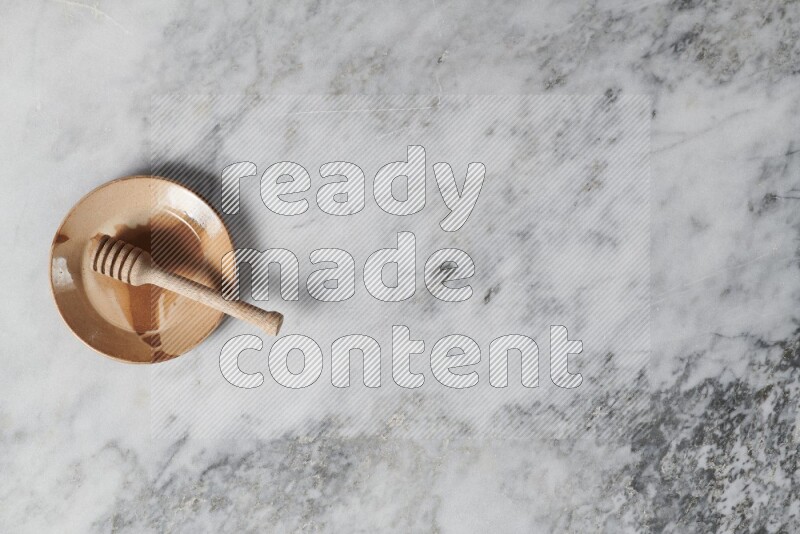 Multicolored pottery plate with wooden honey dipper in it on grey marble background