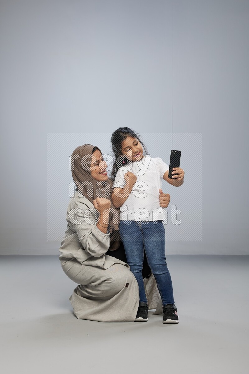 A girl standing taking selfie with her mother on gray background