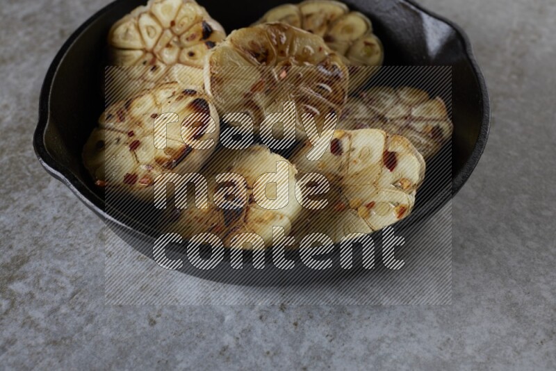 half's roasted garlic in a black pan on a grey textured countertop