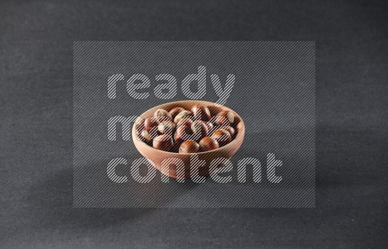 A wooden bowl full of hazelnuts on a black background in different angles
