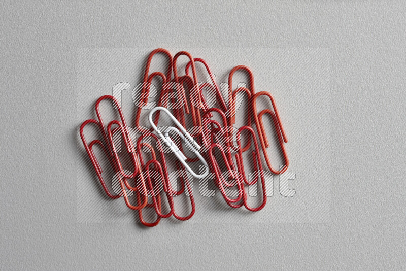 A bunch of red paper clips with a different colored paper clip in the center on grey background