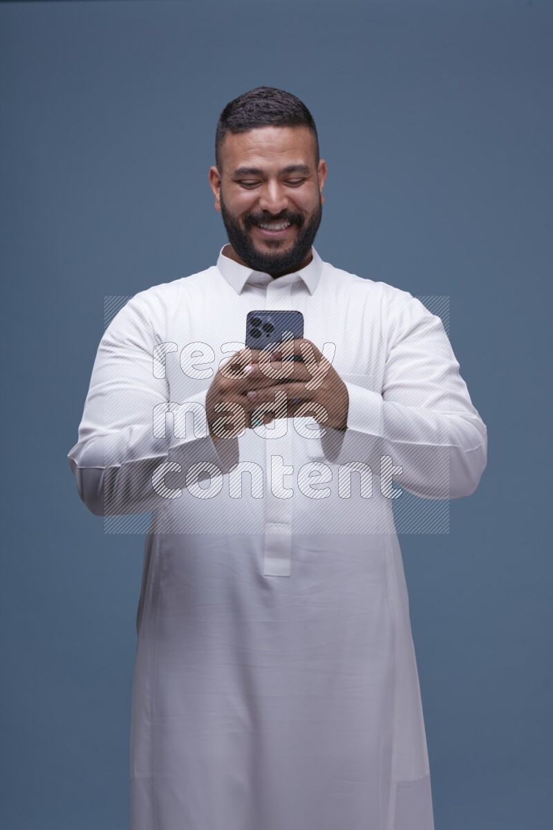 A man Texting on Blue Background wearing Saudi Thob