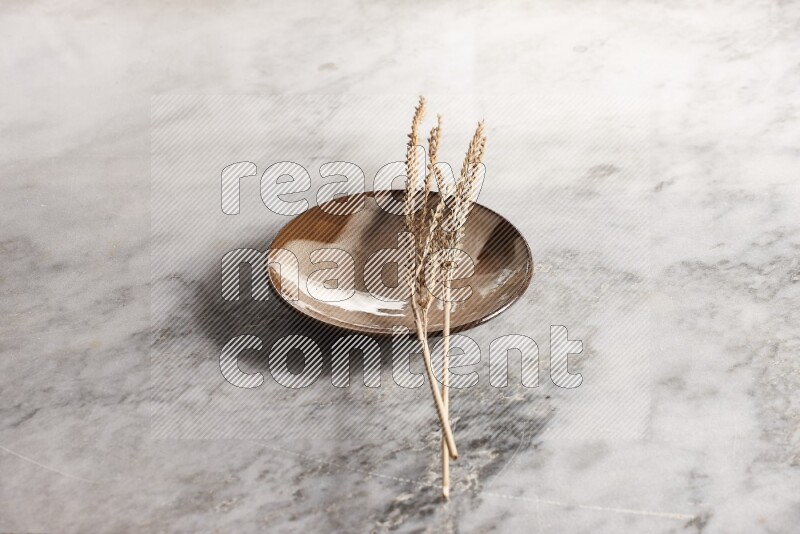 Wheat stalks on multicolored pottery plate on grey marble background