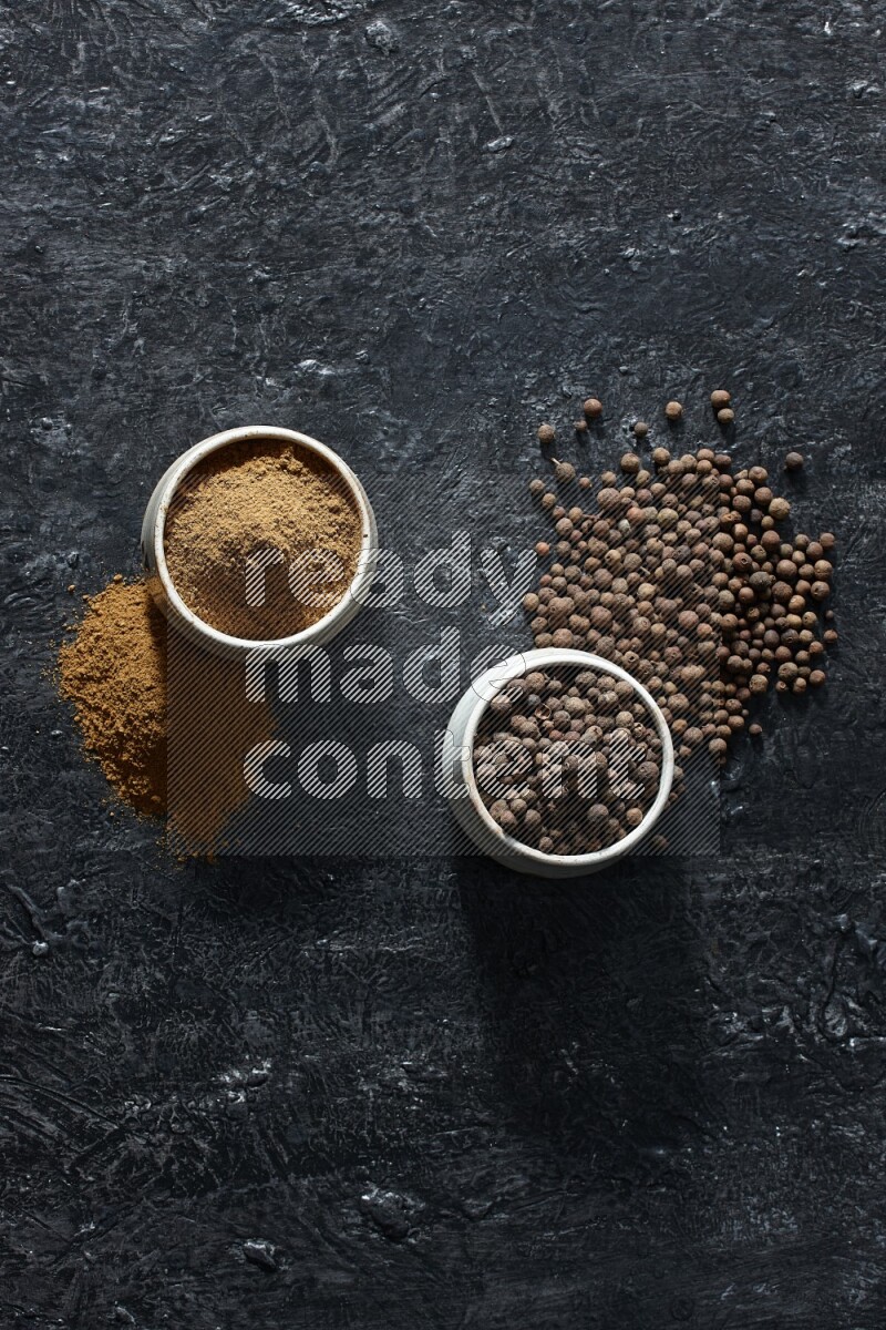 وعاءان بيج، أحدهما ممتلئ ببودرة بهار الفلفل الحلو والآخر بالحبوب وكلاهما متناثران على خلفية سوداء