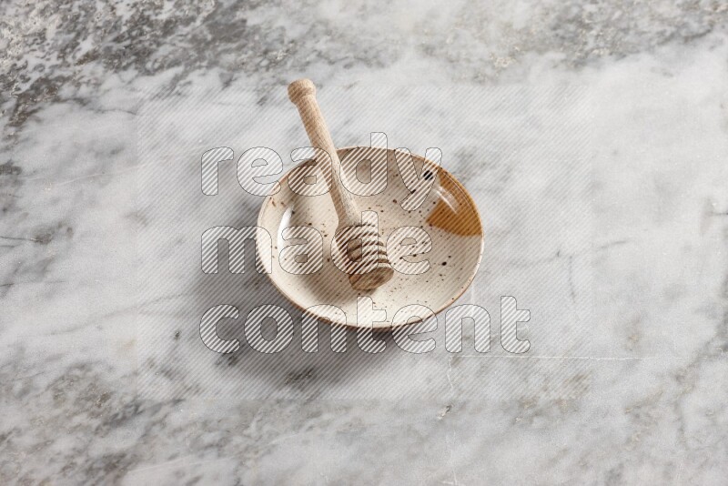 Multicolored pottery plate with wooden honey dipper in it on grey marble background