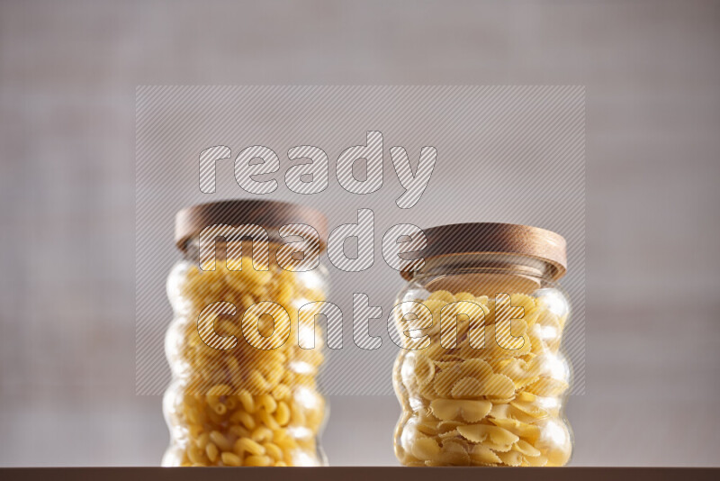 Raw pasta in glass jars on beige background