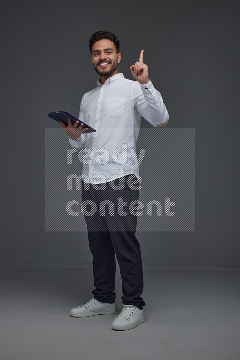 A man wearing smart casual standing and using his tablet and making multi hand gestures eye level on a gray background