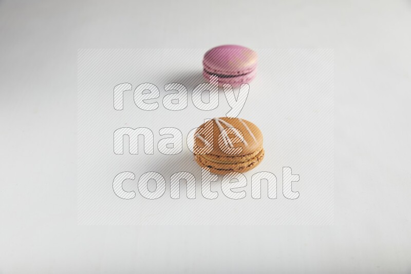 45º Shot of of two assorted Brown Irish Cream, and Purple Strawberry macarons on white background