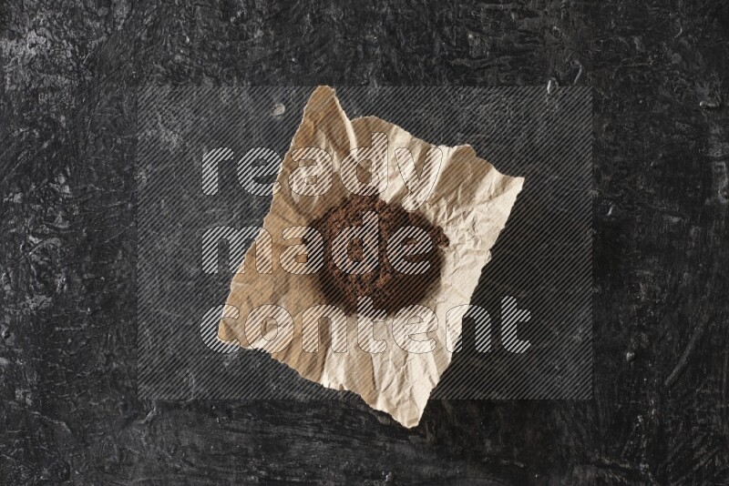 Cloves powder in crumpled piece of paper on a textured black flooring