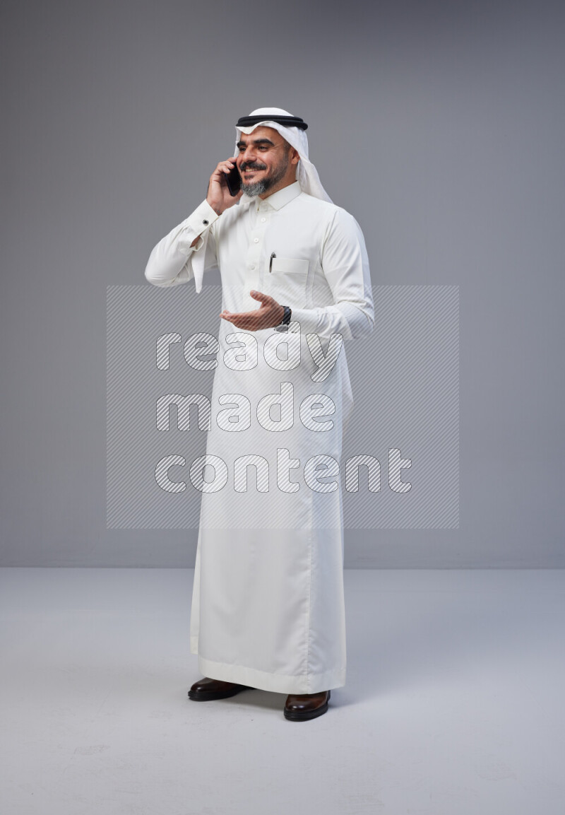 Saudi man Wearing Thob and white Shomag standing talking on phone on Gray background