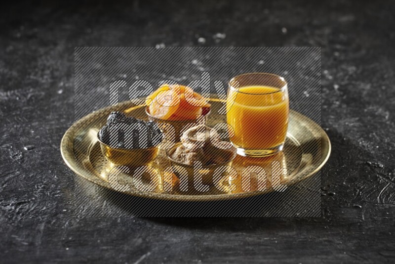 Dried fruits in metal bowls with qamar eldin on a tray in dark setup