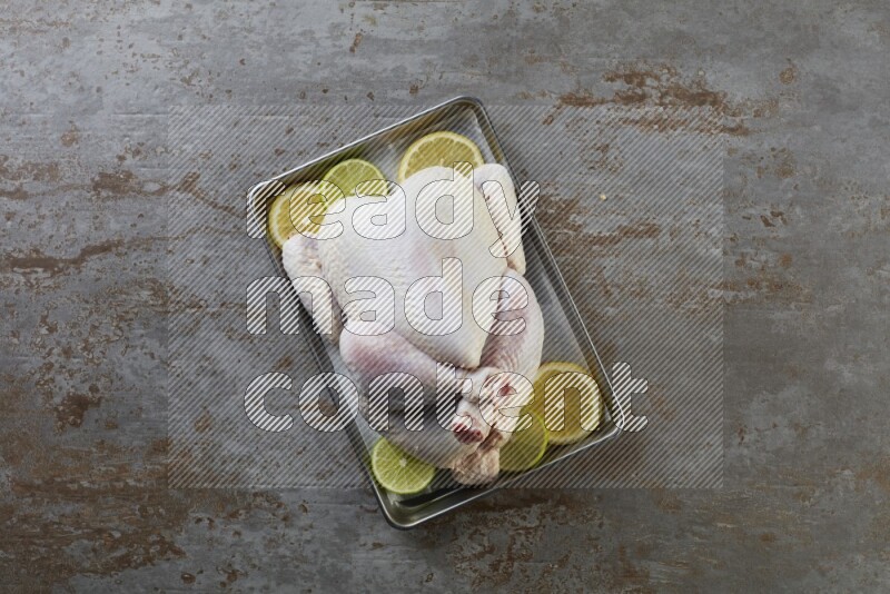 whole Raw chicken on a small oven trey direct on a rustic grey background