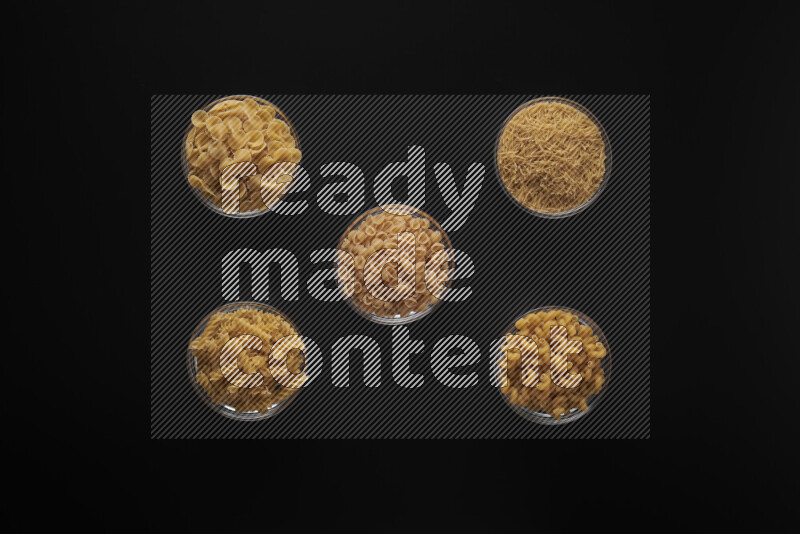 Different pasta types in 5 glass bowls on black background