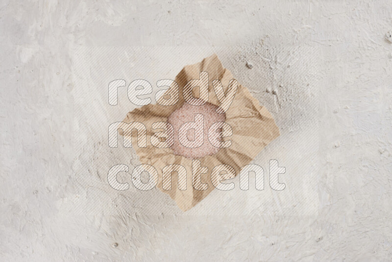 A crumpled piece of paper full of pink himalayan salt on white background