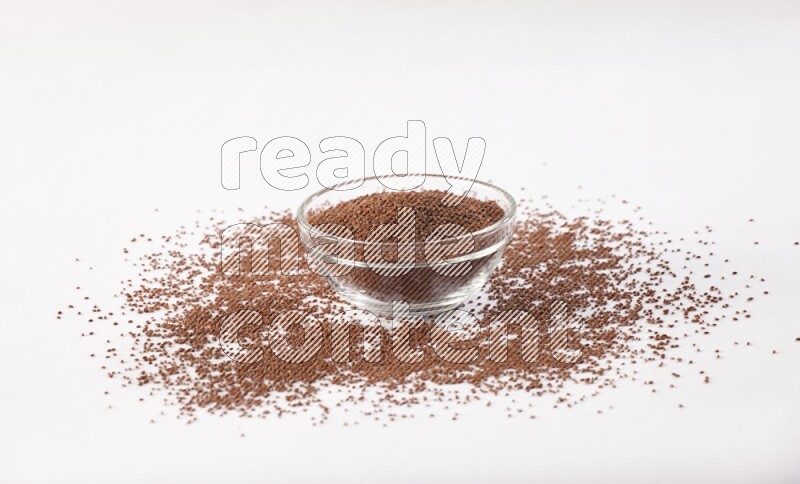 A glass bowl full of garden cress seeds with more seeds spread on a white flooring
