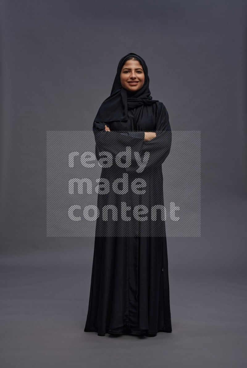 Saudi woman wearing Abaya standing with crossed arms on gray background