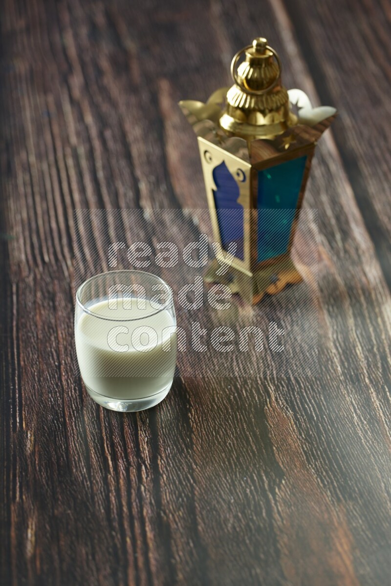 A golden lantern with different drinks, dates, nuts, prayer beads and quran on brown wooden background