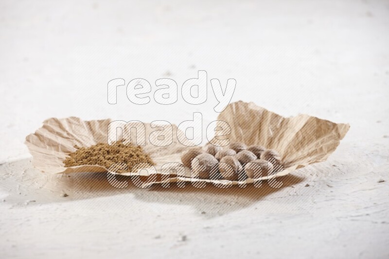 قطعتان من الورق المجعد ممتلئتان بحبوب وبودرة جوزة الطيب علي خلفية بيضاء