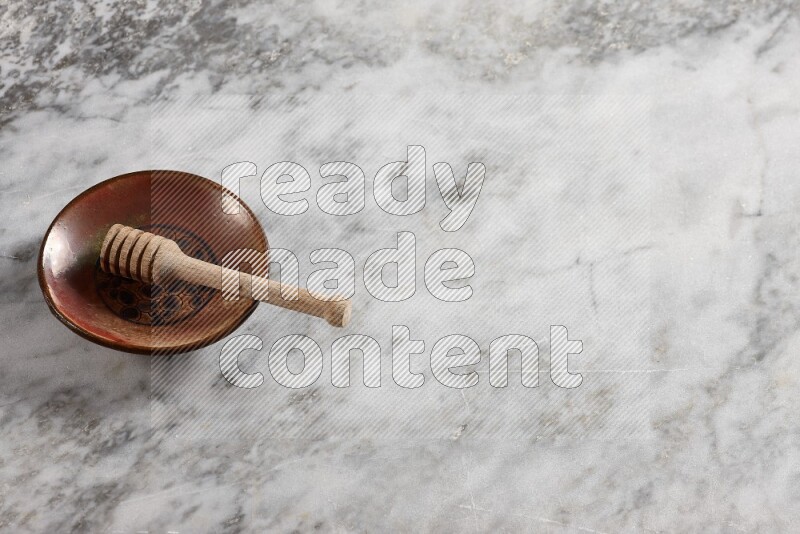 Decorative pottery plate with wooden honey dipper in it on grey marble background