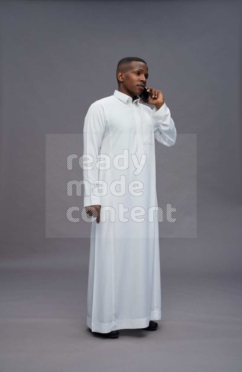 Saudi man wearing thob standing talking on phone on gray background