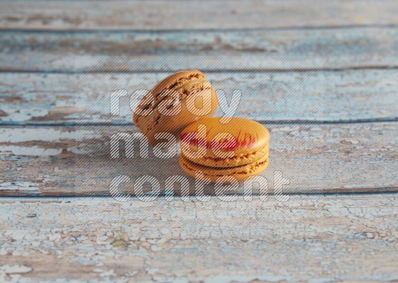 45º Shot of of two assorted Brown Irish Cream, and Orange Exotic macarons on light blue background