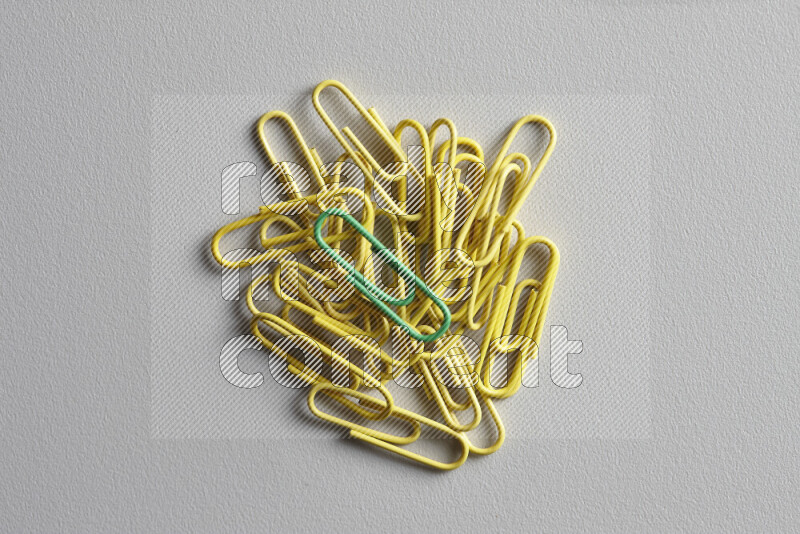 A bunch of yellow paper clips with a different colored paper clip in the center on grey background