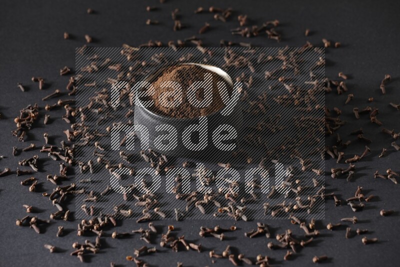 A black pottery bowl full of cloves powder and cloves whole grains on a black flooring