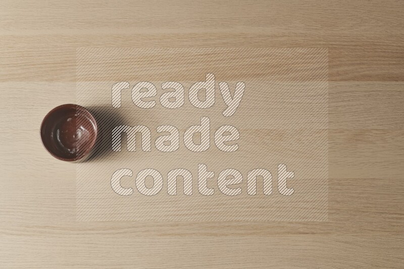 A brown pottery bowl on light wooden background