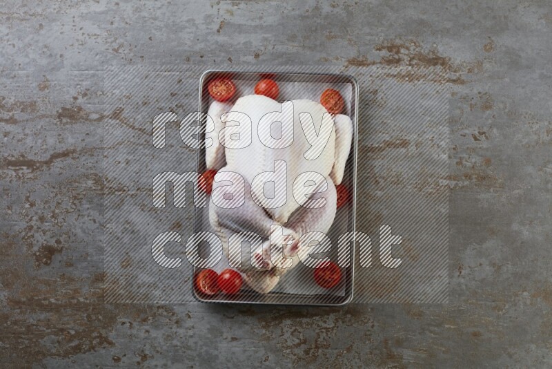 whole Raw chicken on a small oven trey direct on a rustic grey background