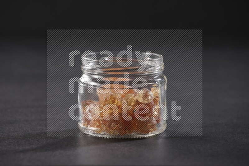 A glass jar full of gum arabic on black flooring