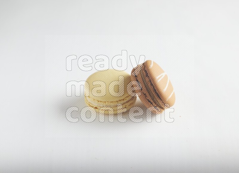 45º Shot of of two assorted Brown Irish Cream, and Yellow Vanilla macarons on white background
