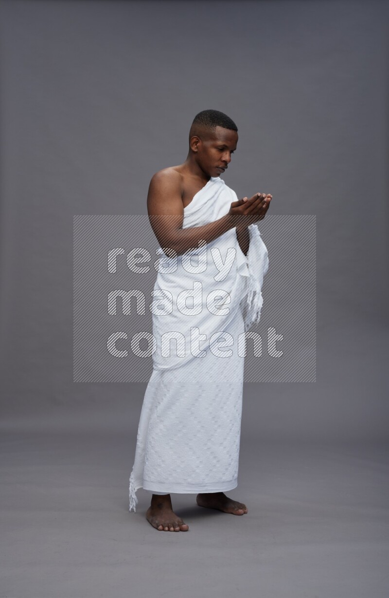 A man wearing Ehram Standing dua'a on gray background