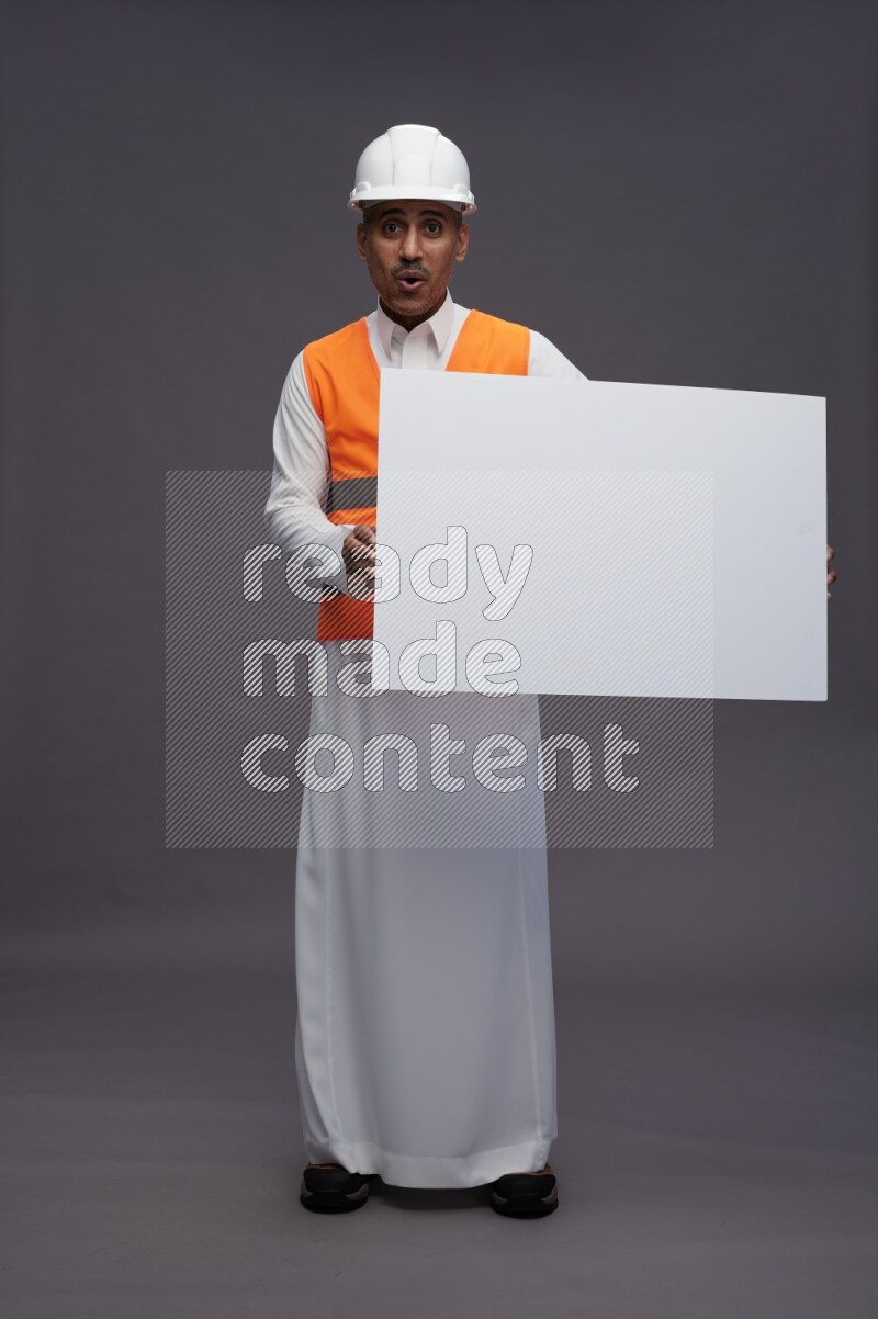 Saudi man wearing thob with engineer vest standing holding board on gray background