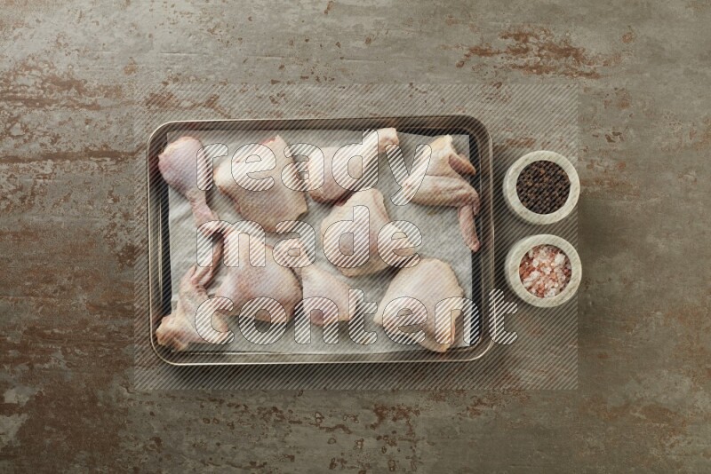 Mixed fresh chicken pieces in an oven tray on a textured rustic background