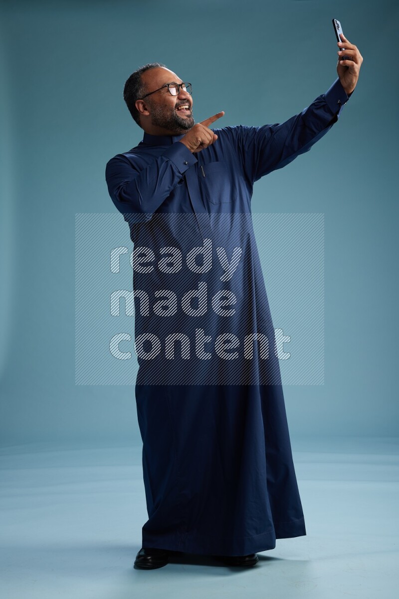 Saudi Man without shimag Standing taking selfie on blue background