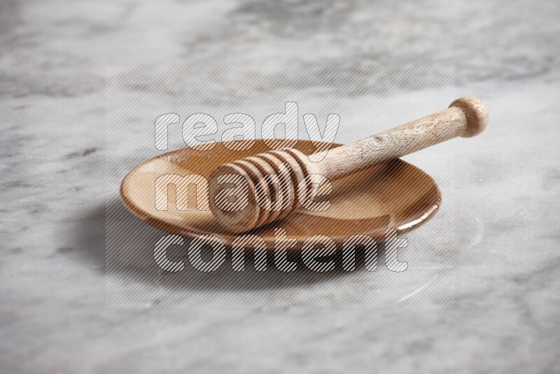 Multicolored pottery plate with wooden honey dipper in it on grey marble background