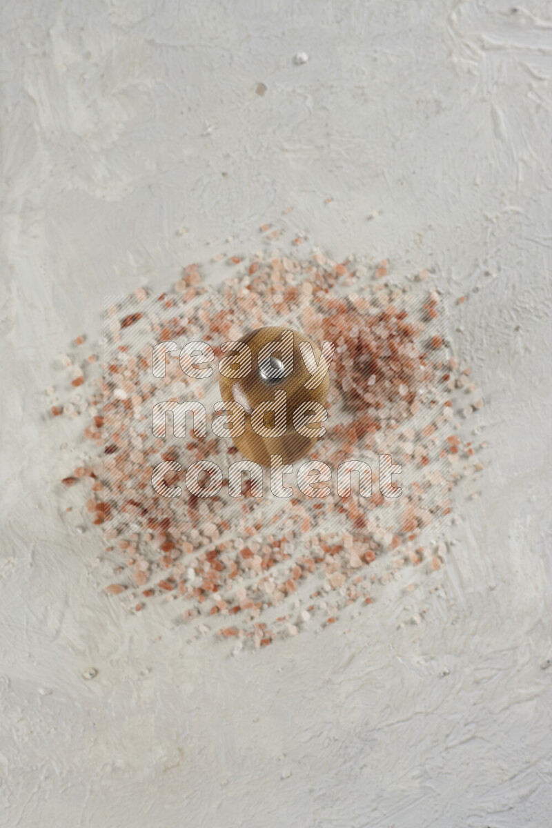 A wooden grinder standing upright and surrounded by coarse pink himalayan salt on white background