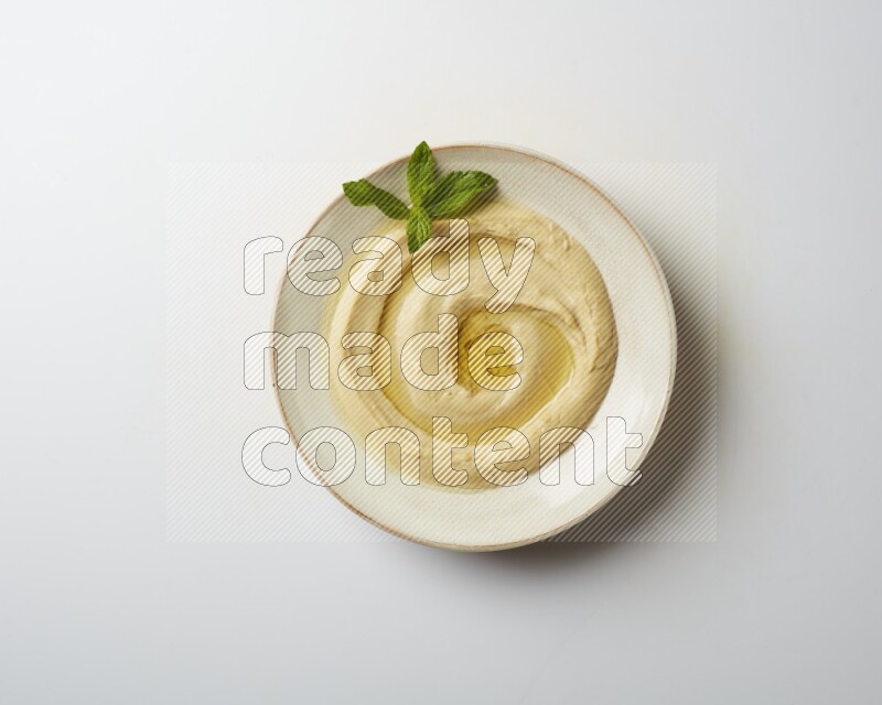 Hummus in a pottry plate garnished with mint  on a white background