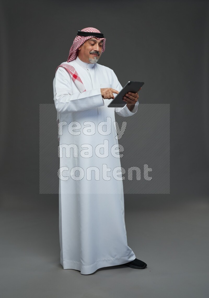 Saudi man with shomag Standing working on tablet on gray background