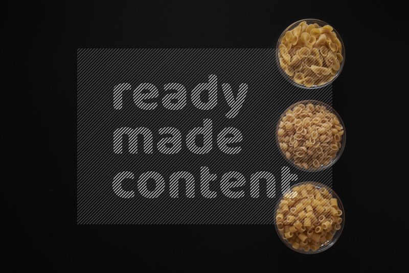 Different pasta types in 3 glass bowls on black background