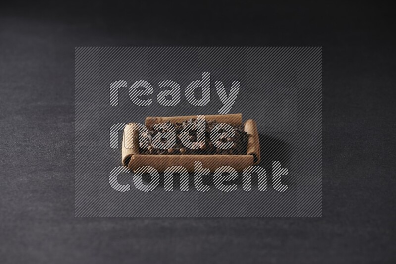 A single square of cinnamon sticks full of cloves on black flooring