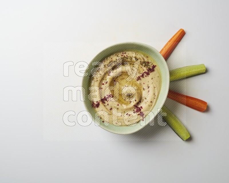 Hummus in a green plate garnished with zattar & sumak on a white background