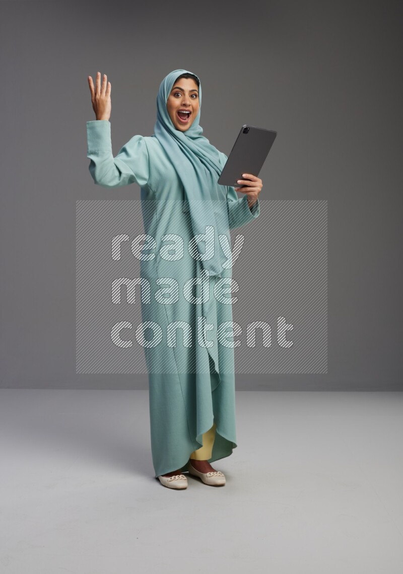 Saudi Woman wearing Abaya standing working on tablet on Gray background