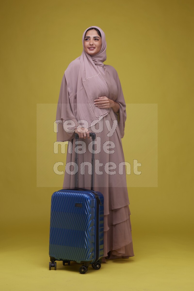A woman With suit Case on a Yellow Background wearing Brown Abaya with Hijab