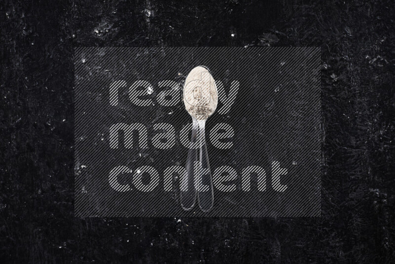 Two metal spoons full of onion powder on black background