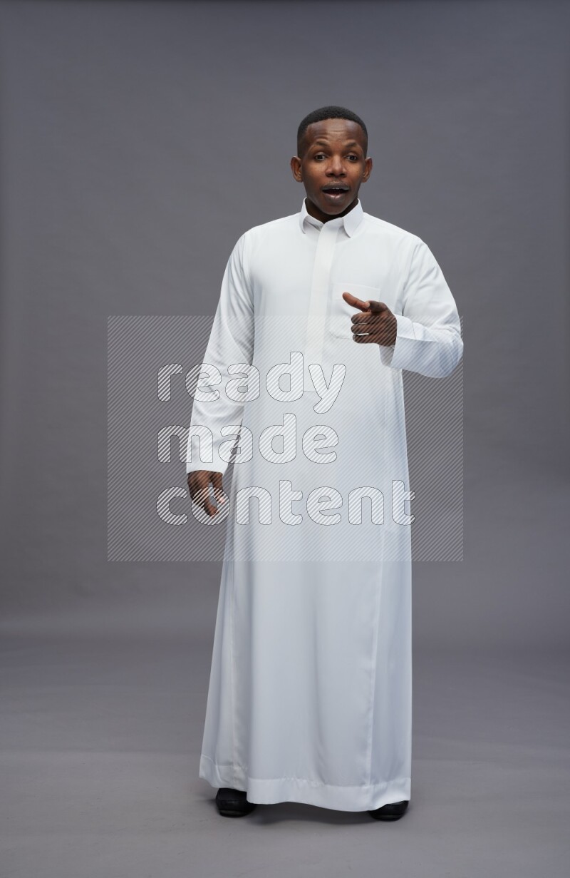 Saudi man wearing thob standing interacting with the camera on gray background