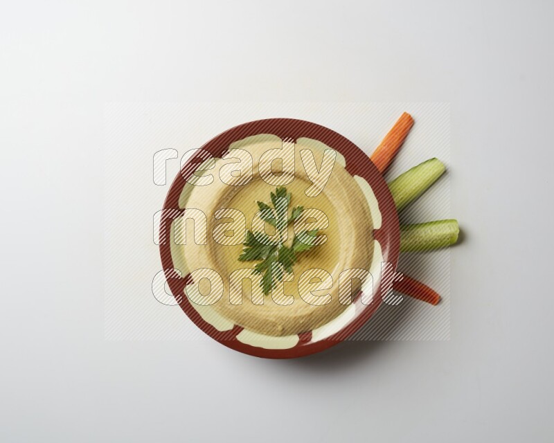 Hummus in a traditional plate garnished with parsley on a white background