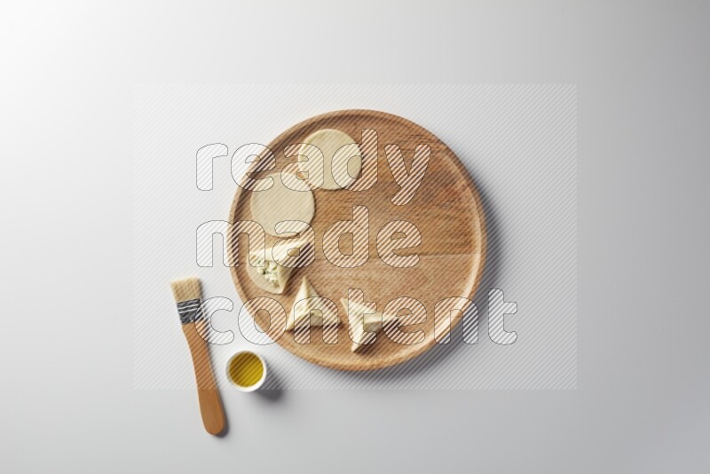 two closed sambosas and one open sambosa filled with cheese while oil with oil brush aside in a wooden dish on a white background