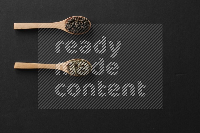 wooden spoons filled with white peppers, cloves, cardamom, salt, black peppers and basil on black flooring