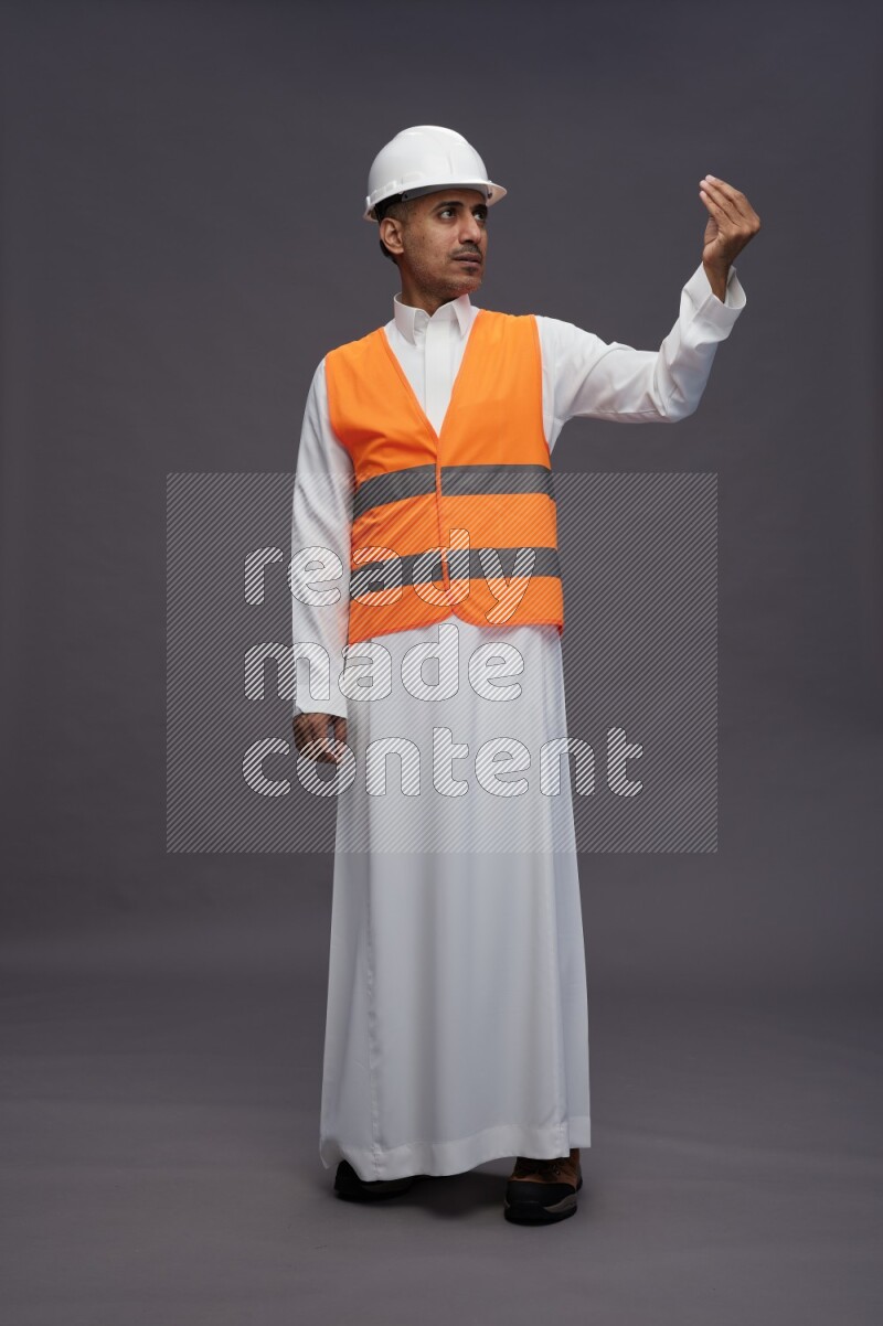 Saudi man wearing thob with engineer vest standing interacting with the camera on gray background